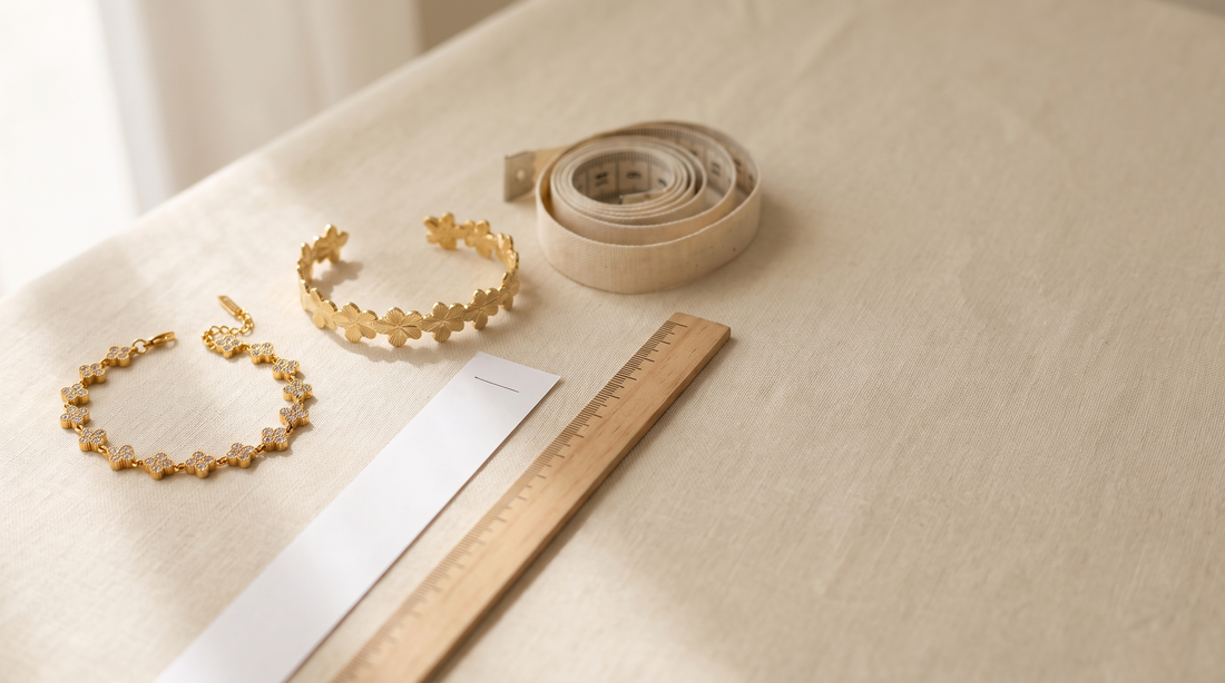 Feines goldfarbenes Armband und offener Armreif aus Edelstahl liegen neben einem Papierstreifen, einem Lineal und einem Maßband
