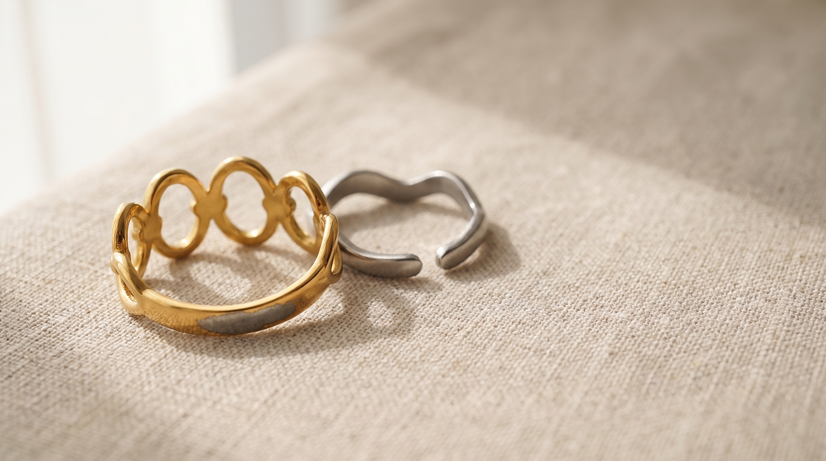 Zwei Ringe auf beigem Leinen: links ein goldfarbener Ring, dessen Vergoldung an der Innenseite bis auf graues Metall durchgerieben ist, rechts ein blanker Edelstahlring
