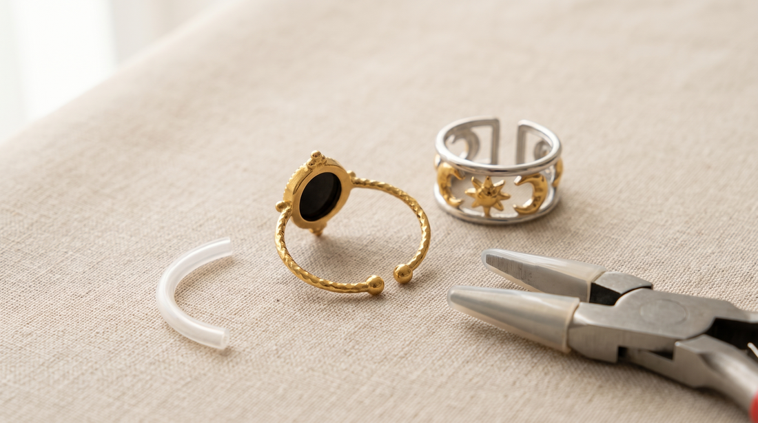 Goldfarbener offener Edelstahlring auf beigem Leinen, der Spalt zwischen den beiden Schienenenden ist deutlich sichtbar; daneben eine Flachzange und eine transparente Silikon-Ringeinlage, dahinter ein unveränderter silberfarbener Ring.