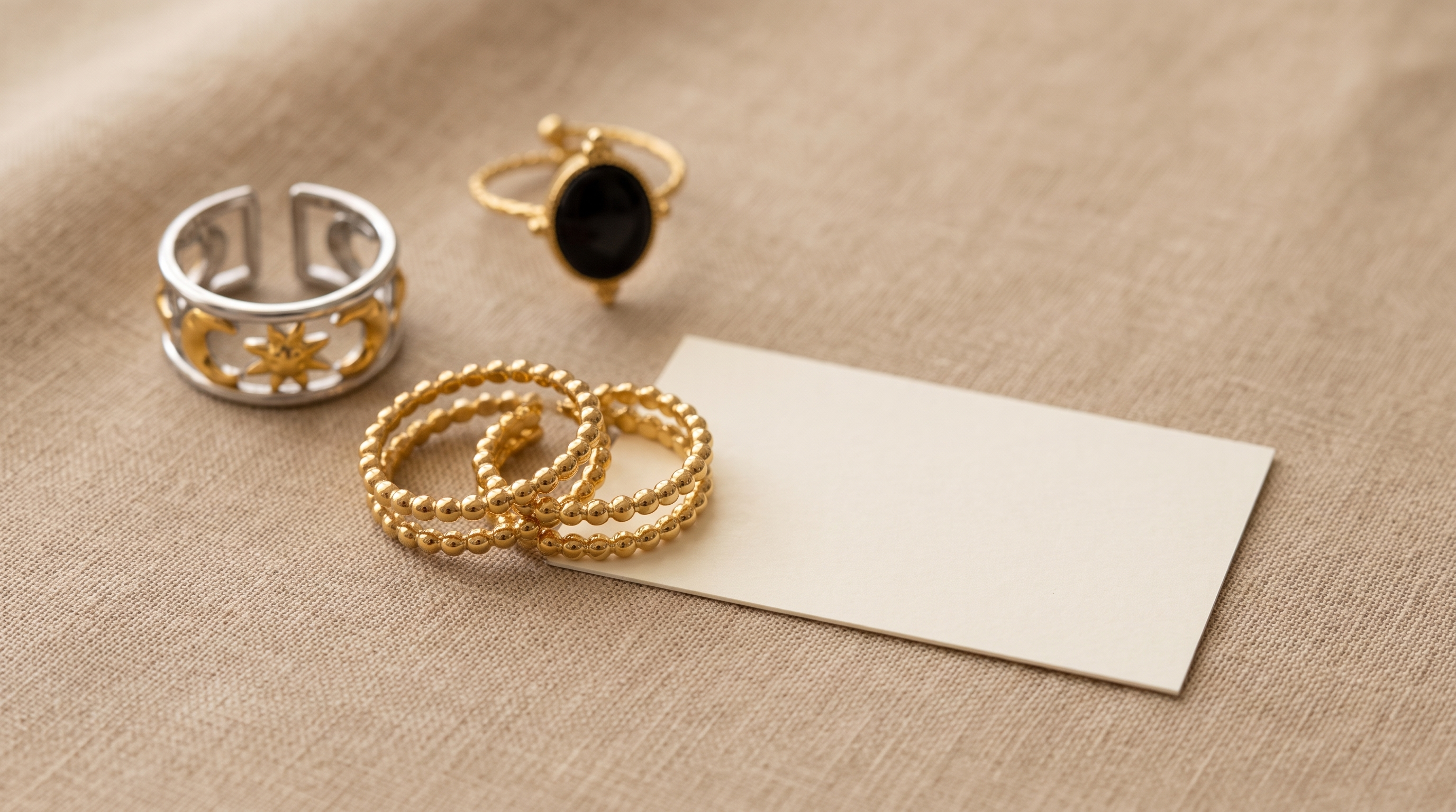 Zwei baugleiche goldfarbene Ringe liegen auf beigem Leinen neben einem leeren, unbedruckten Kärtchen
